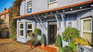 A two-story house with a blue exterior, a black front door, and a small porch with potted plants. - Hooray Henrys Sheringham (Sheringham)