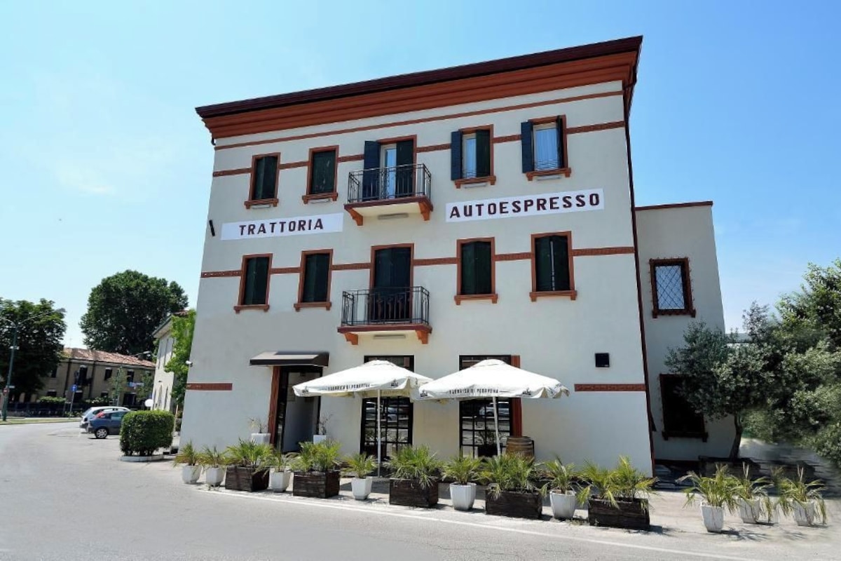 A building with a sign reading 'TRATTORIA AUTOESPRESSO' and outdoor seating with umbrellas.