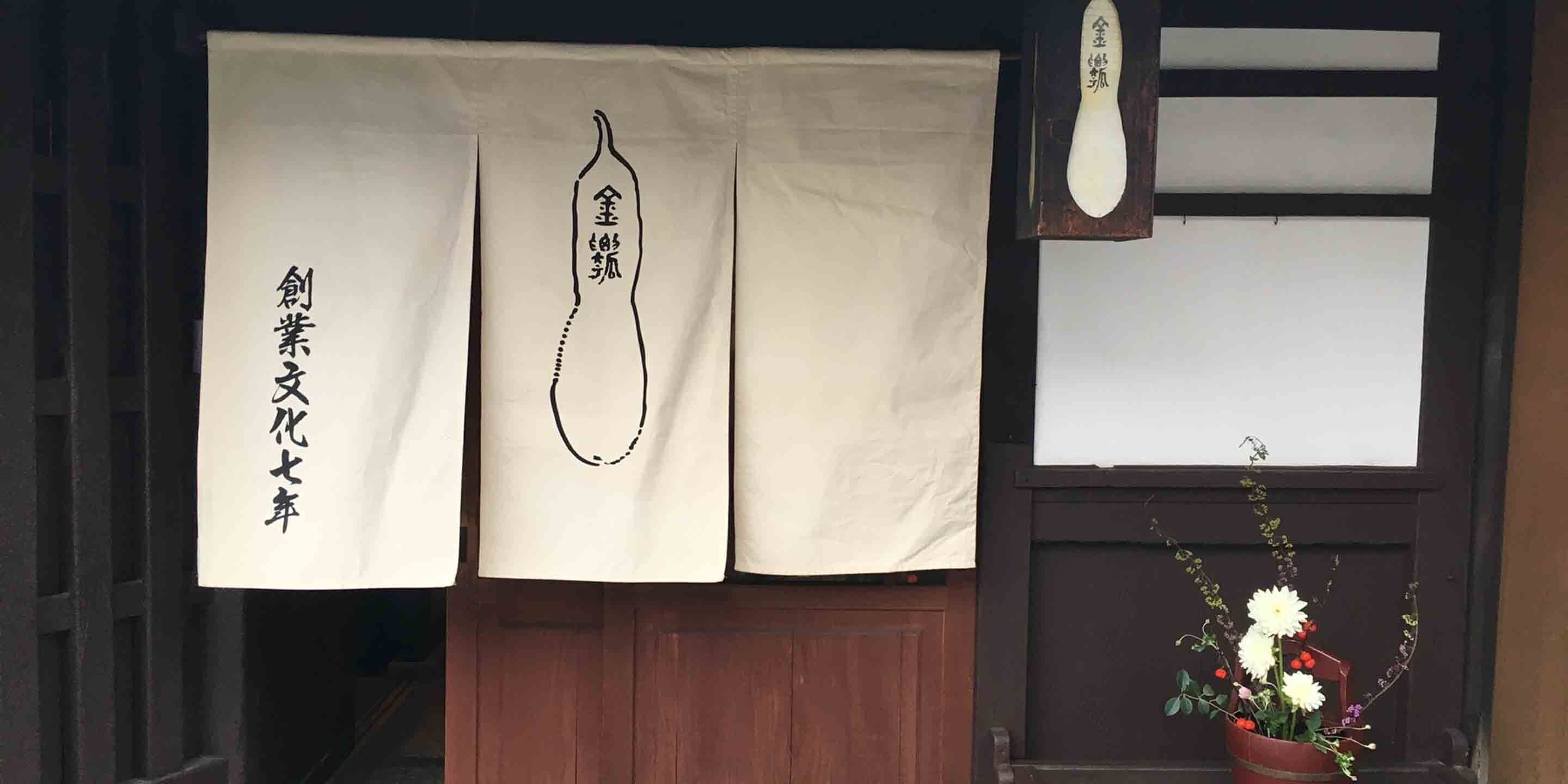 Una entrada tradicional japonesa con puerta de madera, papel blanco con caracteres chinos e ilustración de un pez en un colgante de papel blanco.