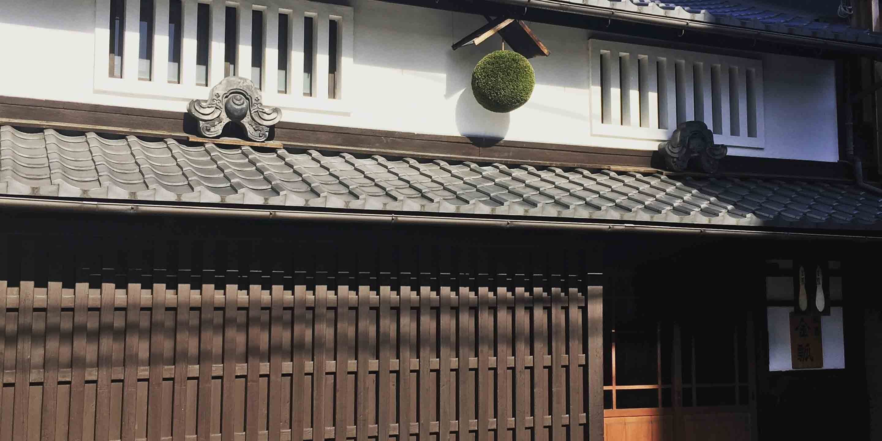 Un edificio japonés tradicional con tejado de tejas, pared de listones de madera y un adorno esférico colgante.