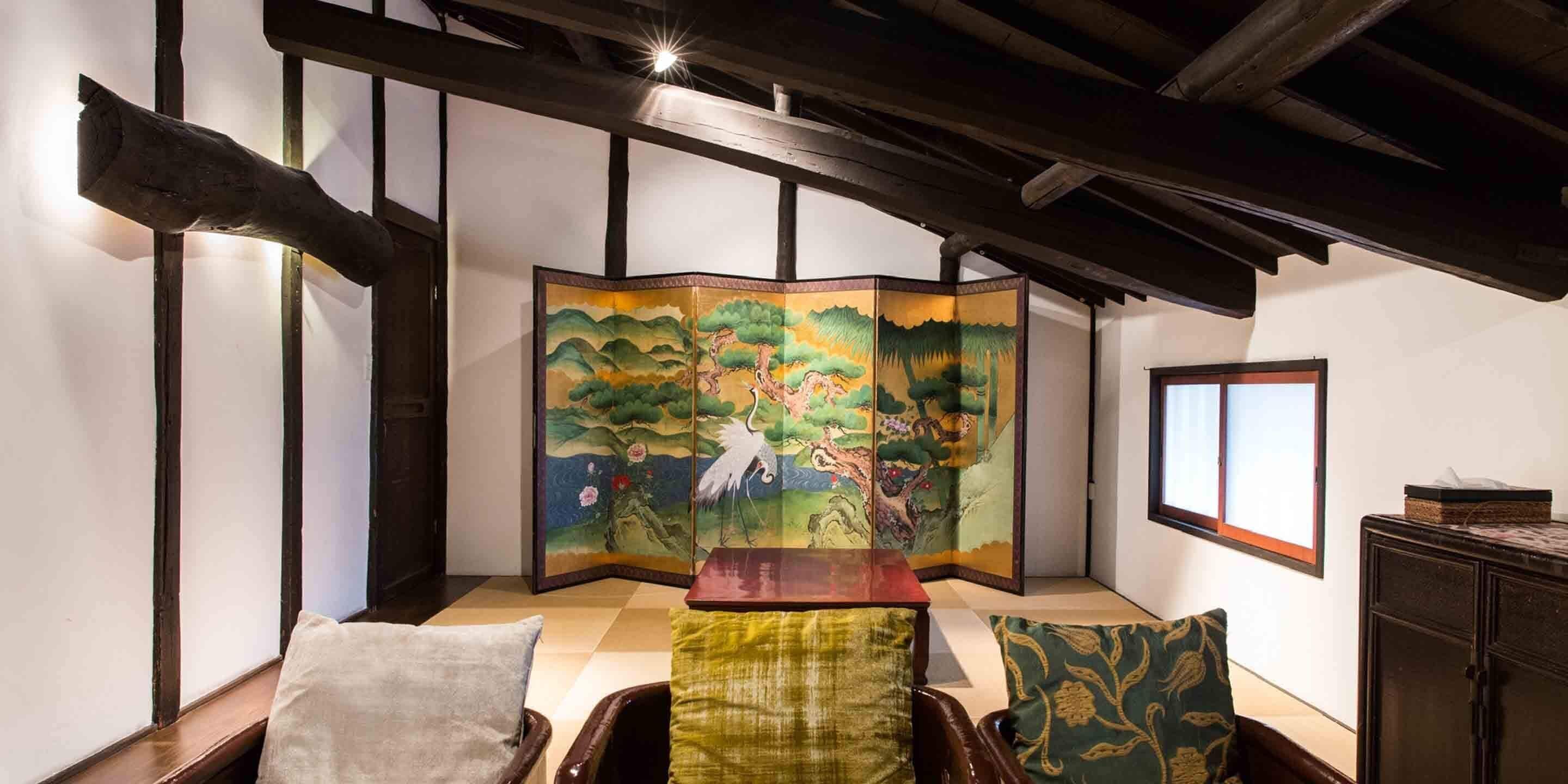 Una habitación tradicional con suelo de tatami, un shoji con una pintura de naturaleza, un armario de madera y una ventana con vistas.