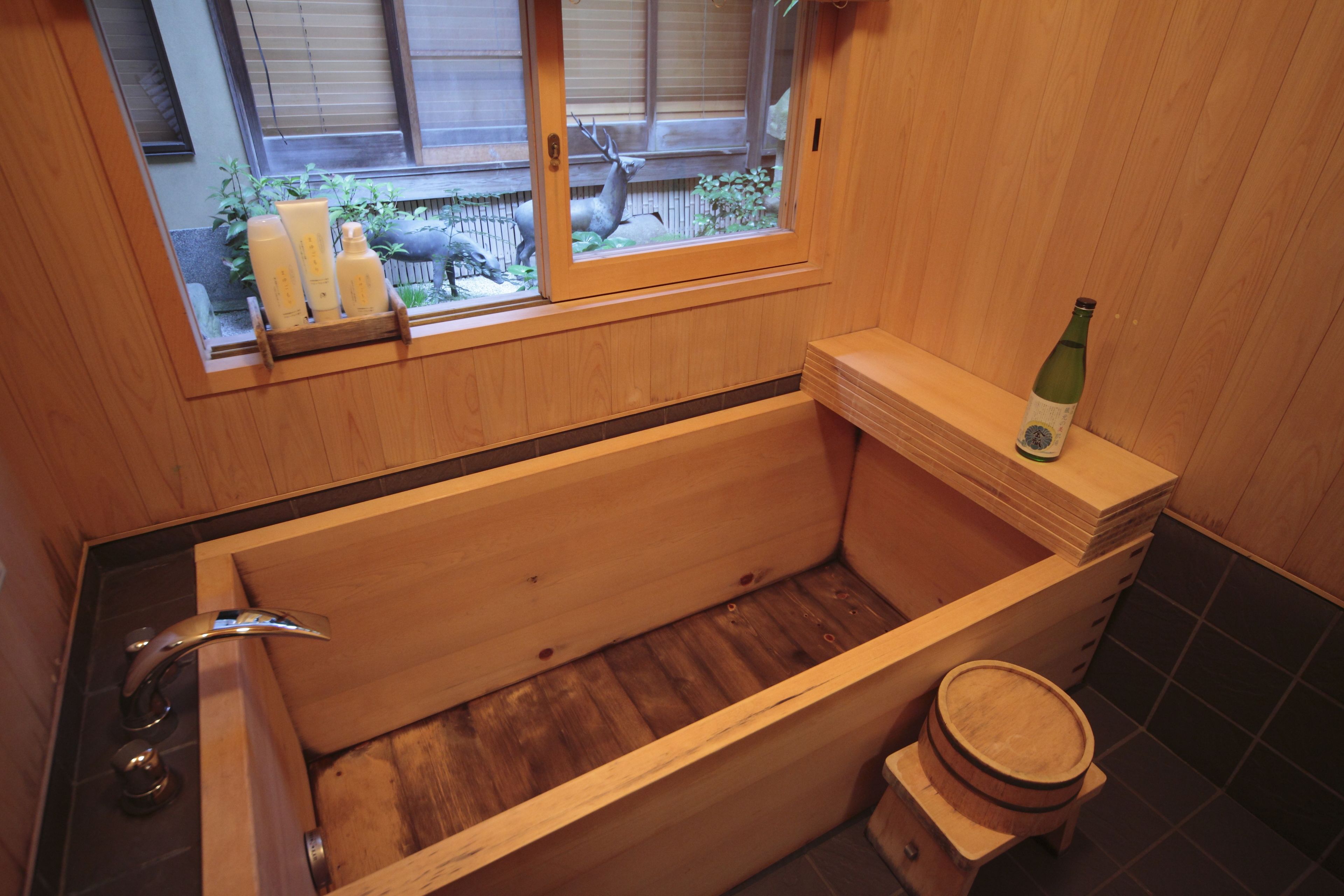 A wooden bathtub with a window, a bottle of wine, and a wooden stool.