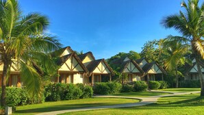 A row of thatched-roof cottages with a paved pathway and lush greenery. - Playa Venao Hotel Resort (Las Escobas del Venado)