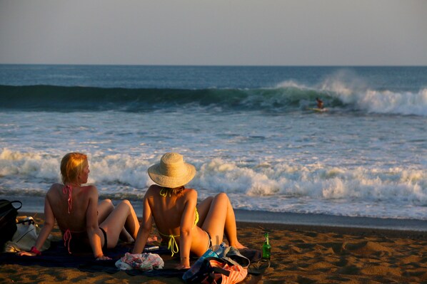 Two people sitting on a beach towel, facing the ocean.