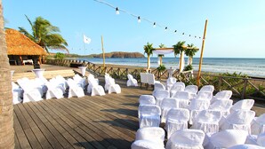 A wooden deck with white chairs and tables, a thatched-roof building, and a view of the ocean. - Playa Venao Hotel Resort (Las Escobas del Venado)