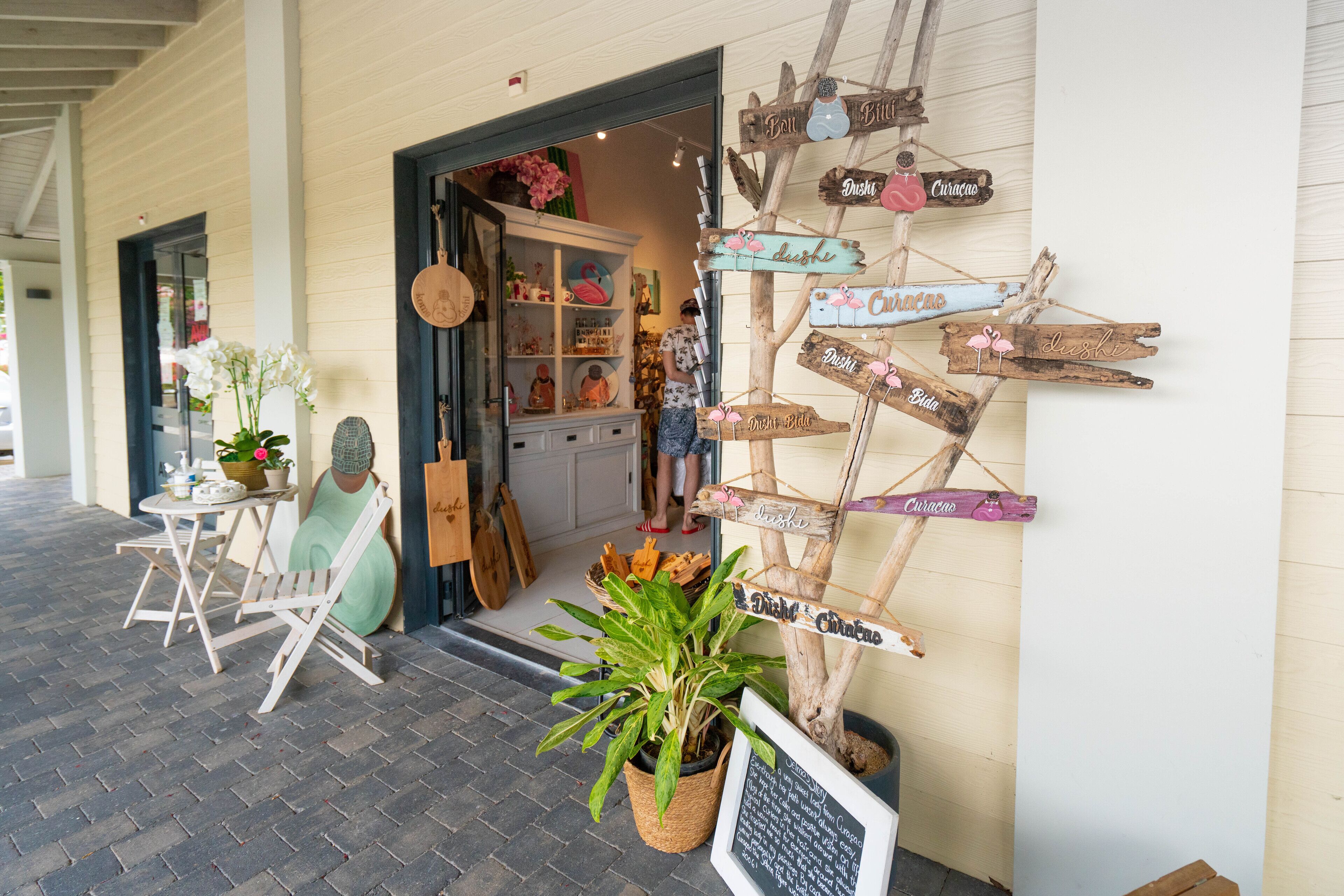A storefront with a wooden signpost with various names, a potted plant, and a chalkboard menu.