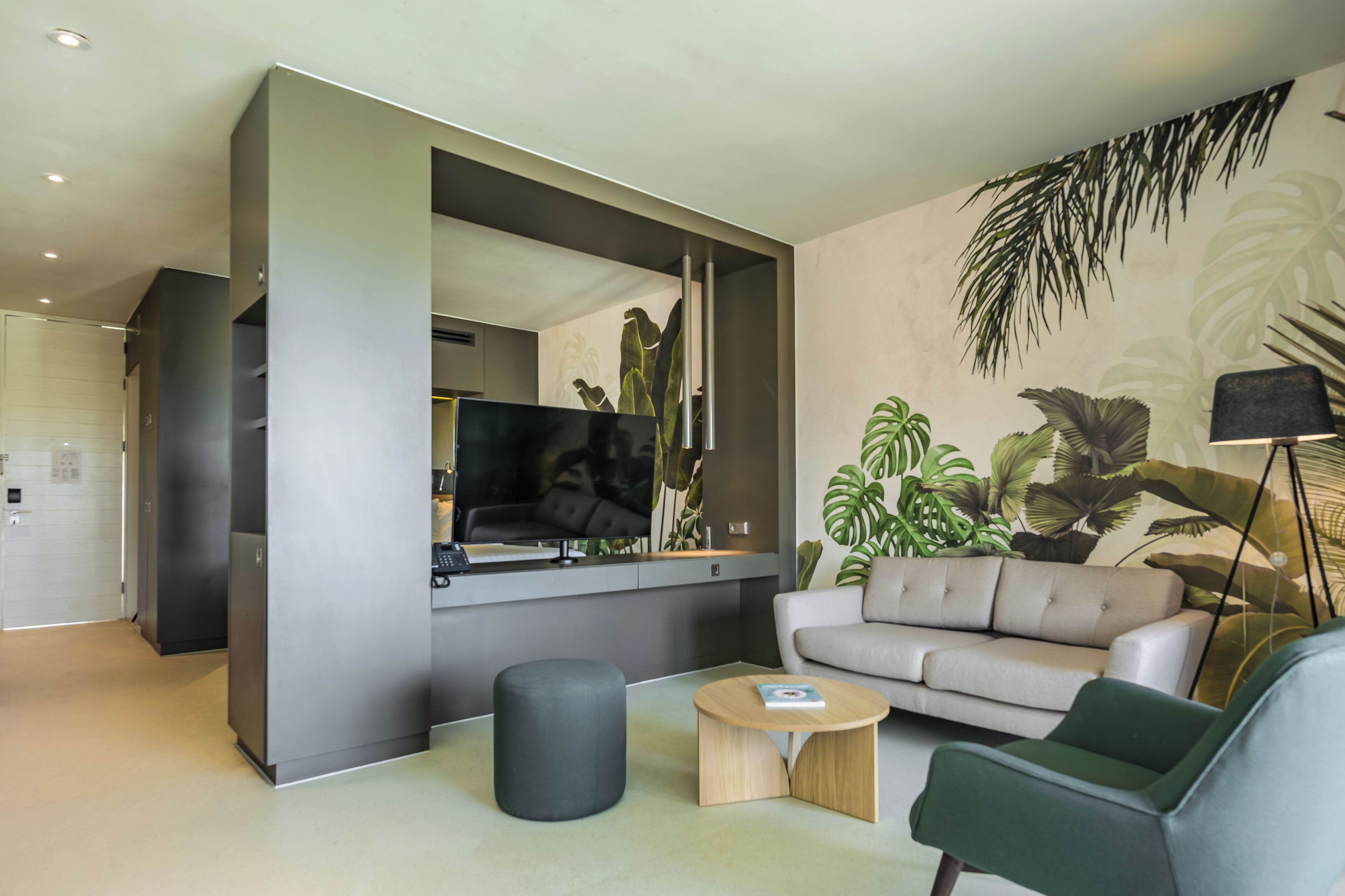 Een moderne woonkamer met een flatscreentelevisie, een grijze bank, een ronde salontafel en een groene fauteuil.