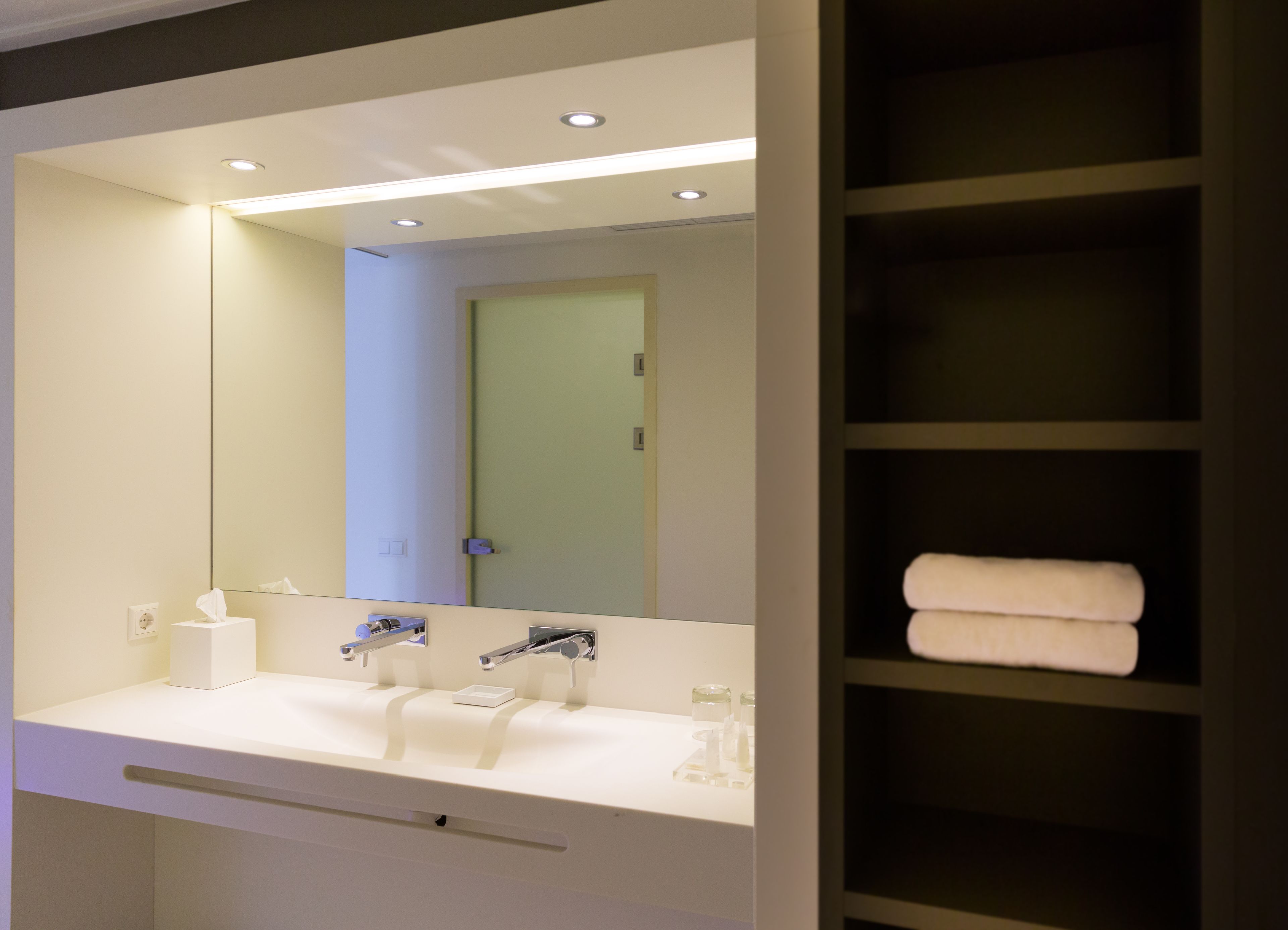 Un bagno moderno con un lavandino bianco, due rubinetti, uno specchio e un porta asciugamani.