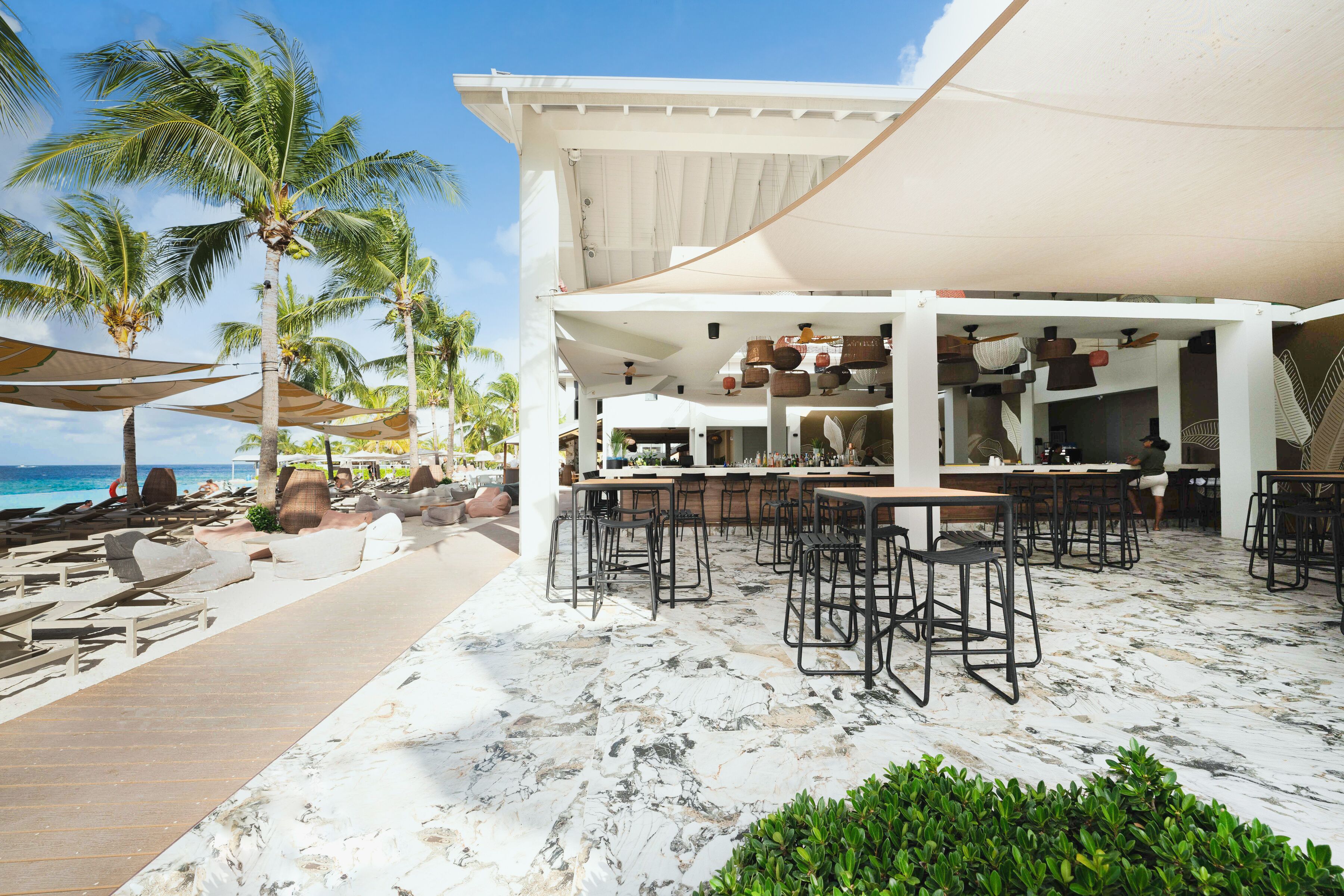 Un restaurant situé en bord de mer, avec une terrasse, des palmiers et une vue sur l’océan.