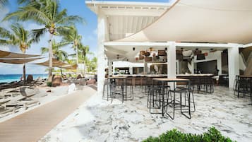 Un restaurant situé en bord de mer, avec une terrasse, des palmiers et une vue sur l’océan.