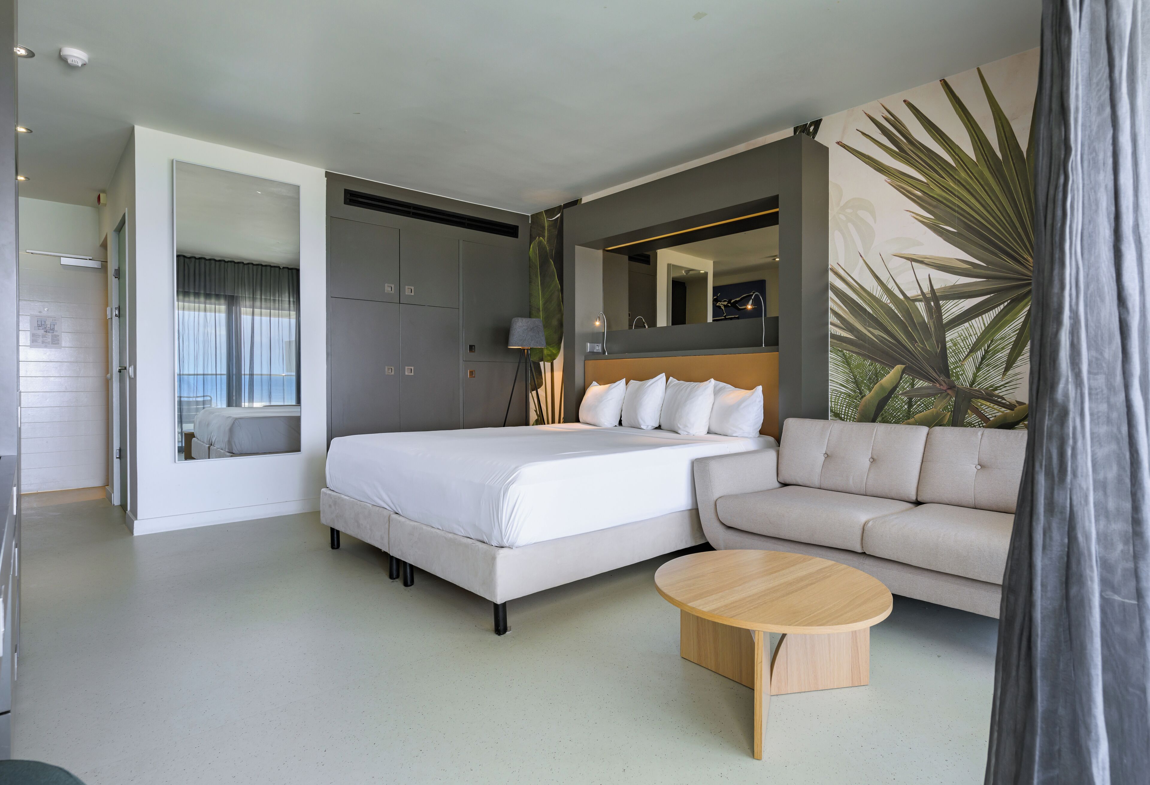 Una habitación de hotel moderna con una cama, un sofá, una mesita de café y un espejo grande.
