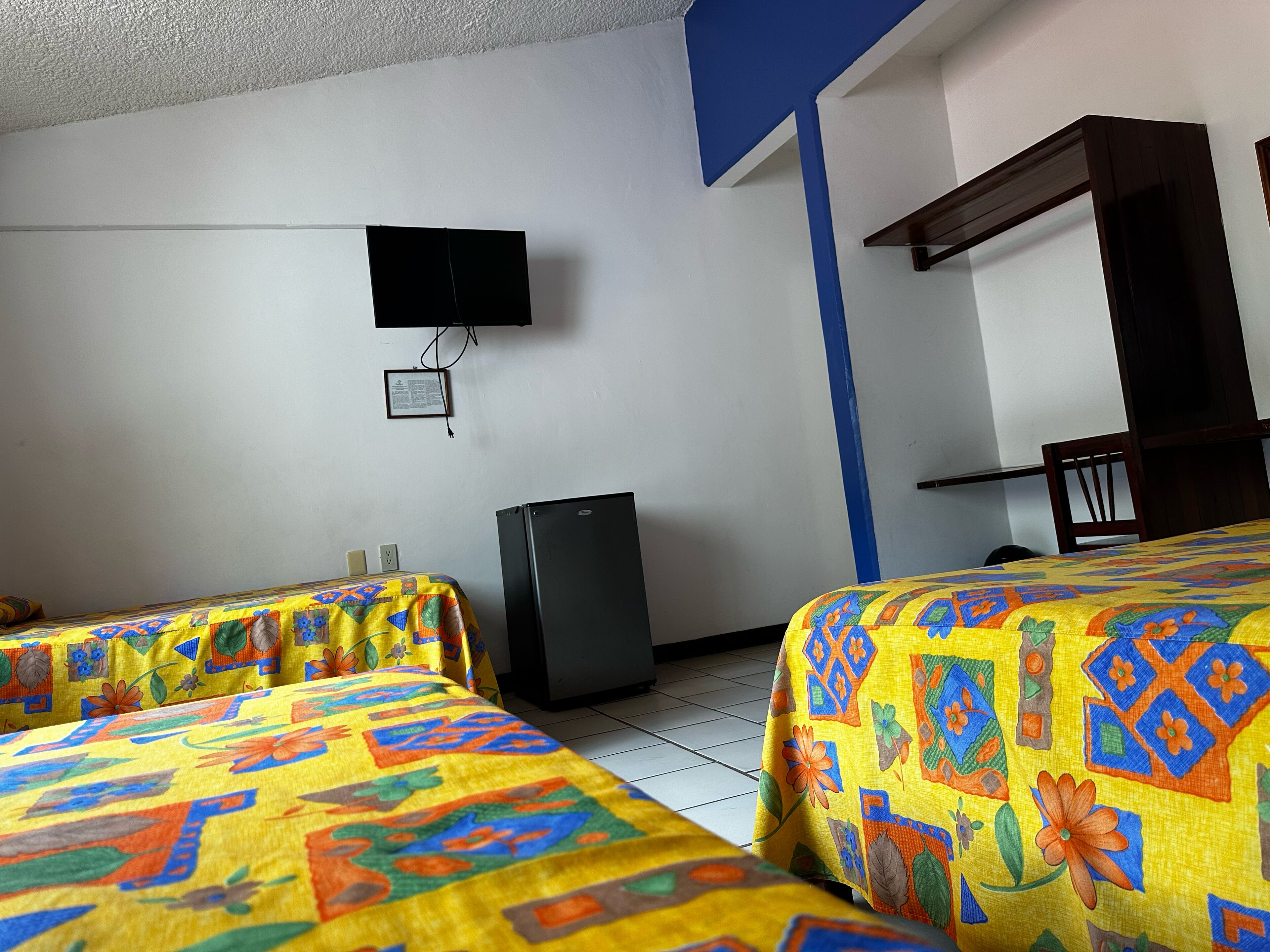 Habitación de hotel con dos camas, televisión, refrigerador y una mesita.