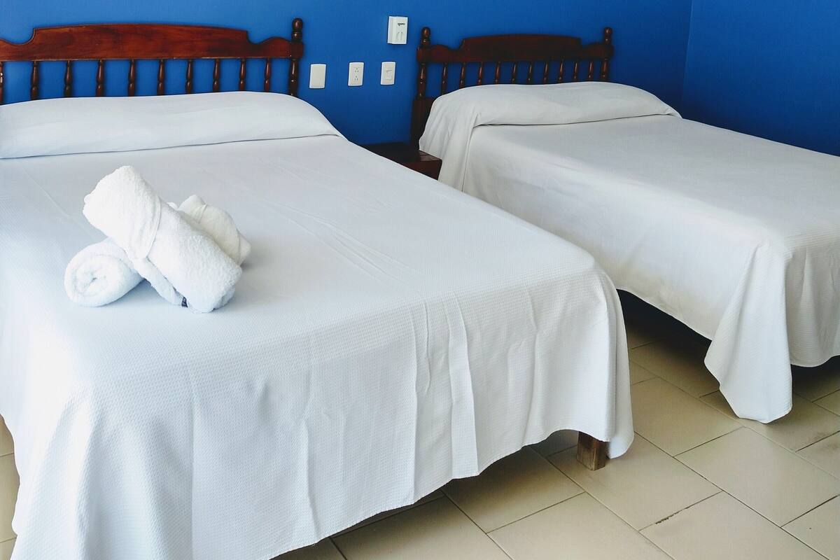 A hotel room with two beds, white linens, and blue walls.