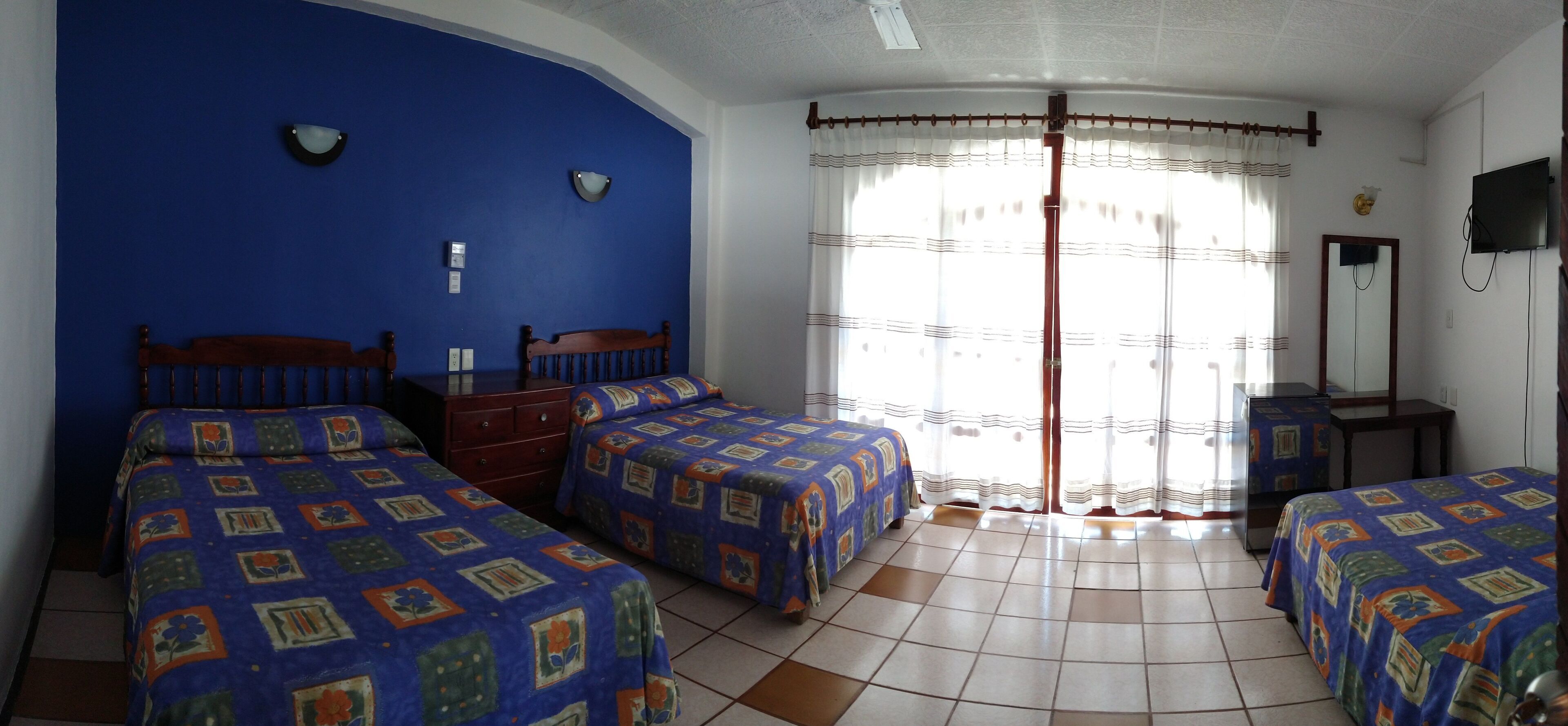 Una habitación con dos camas, un cabecero de madera, una mesita, un espejo y una ventana con cortinas.