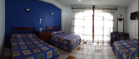 Una habitación con dos camas, un cabecero de madera, una mesita, un espejo y una ventana con cortinas.