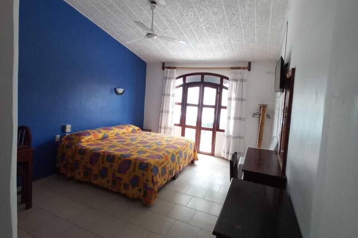 A bedroom with a bed, a desk, and a window with curtains.