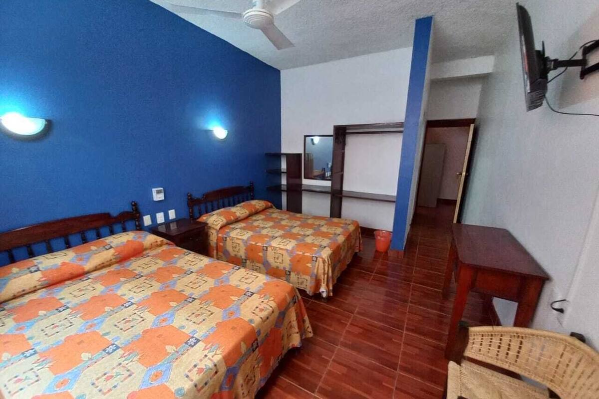A room with two beds, a ceiling fan, a wooden table, and a chair.