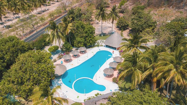 An aerial view of a resort with a large swimming pool, palm trees, and a thatched-roof building. - Hotel & Club Campestre Altos Paraiso (Villa de Tututepec de Melchor Ocampo)