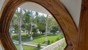 A view through a wooden-framed window of a well-maintained lawn with palm trees, a pathway, and a small building in the background. - Hotel & Club Campestre Altos Paraiso (Villa de Tututepec de Melchor Ocampo)