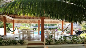 A covered outdoor seating area with chairs and a pool. - Hotel & Club Campestre Altos Paraiso (Villa de Tututepec de Melchor Ocampo)
