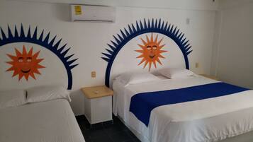 A hotel room with two beds, each with a sun design on the headboard, a small bedside table, an air conditioning unit above the beds, and a ceiling fan.