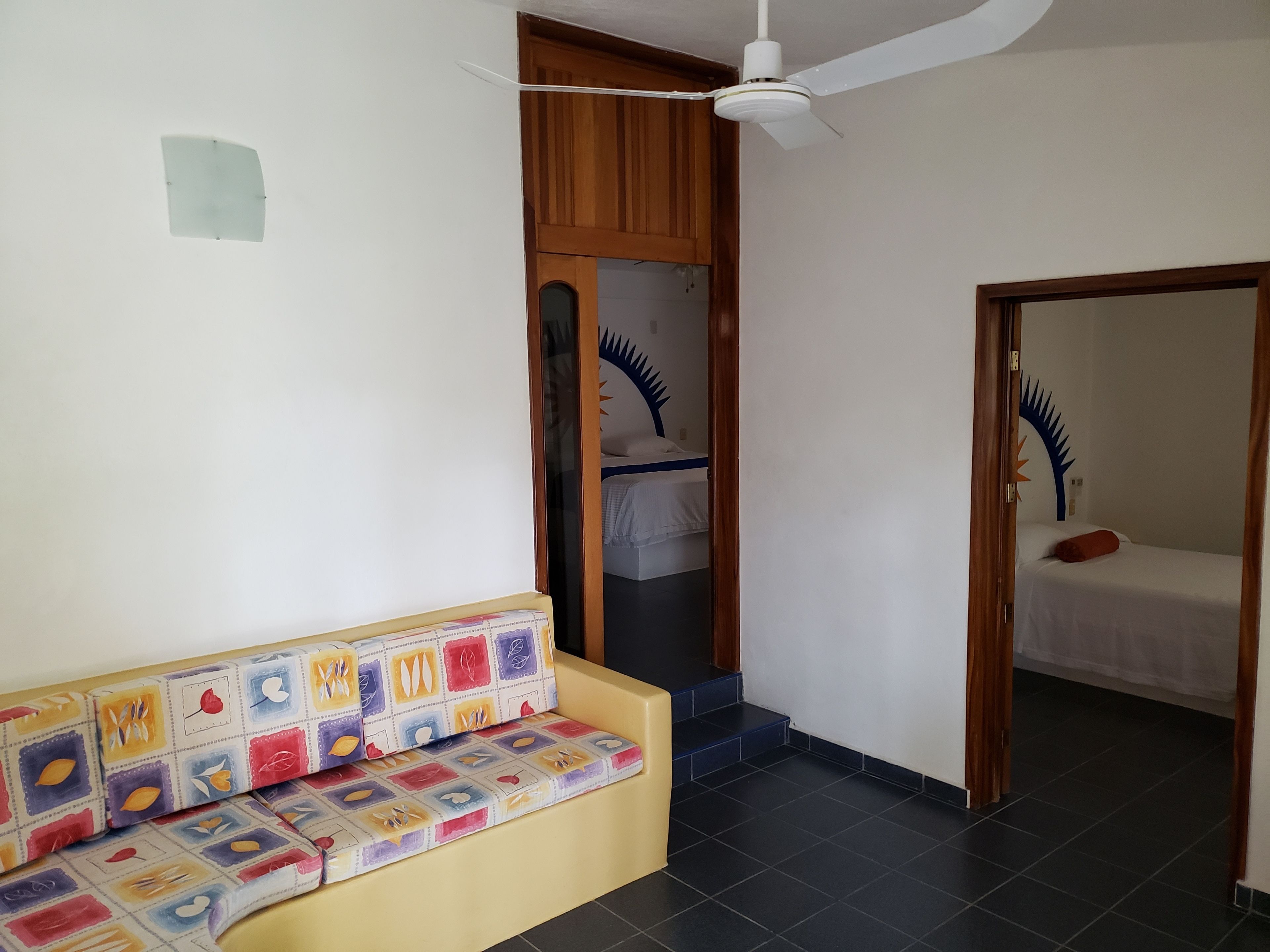 A room with a sofa, a bed, a ceiling fan, and a door leading to another room.