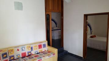 A room with a sofa, a bed, a ceiling fan, and a door leading to another room.