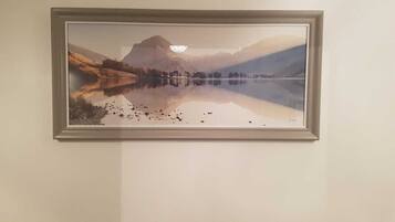 Ein gerahmtes Landschaftsbild mit einem stillen See, Bergen und Bäumen.