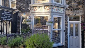 A corner building with a stone facade, a sign for a guest house, and a small garden with lavender. - Bowness Guest House (Windermere)