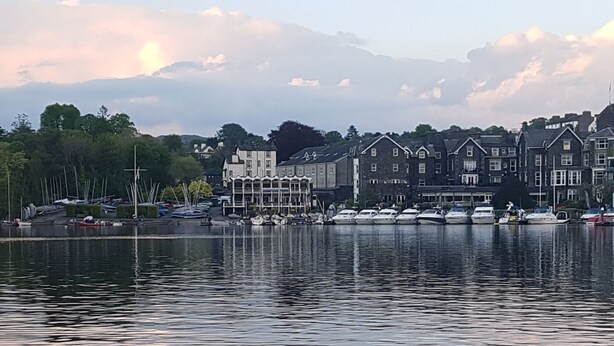 A waterfront view with boats docked, a row of houses, and a calm lake. - Bowness Guest House (Windermere)