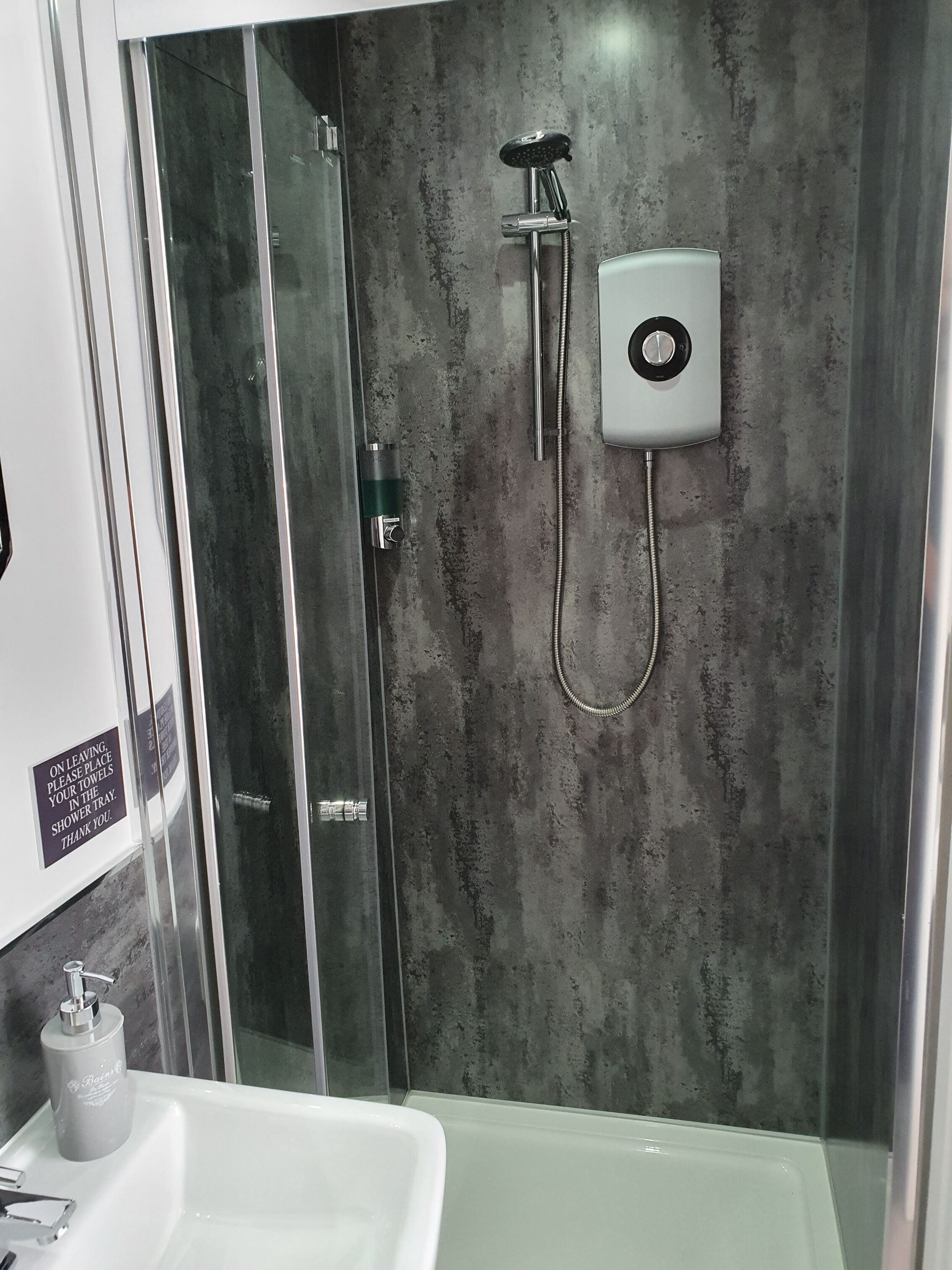 A modern bathroom with a glass-enclosed shower, a white sink, and a shower control panel.