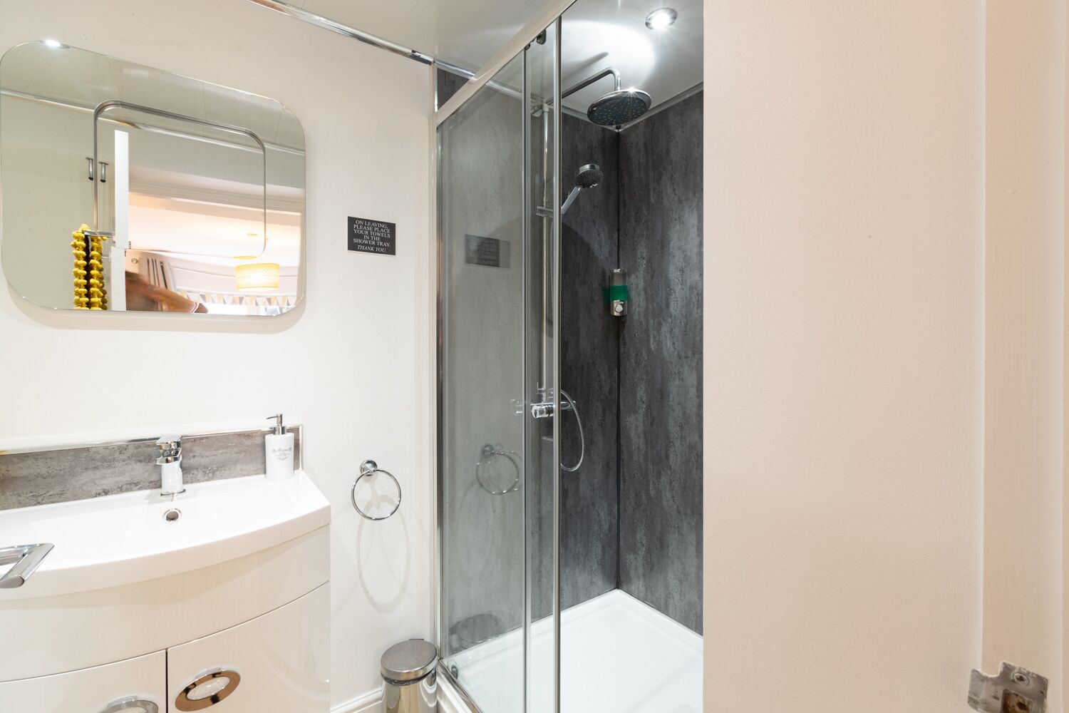 Une salle de bain moderne avec une douche à l’italienne en verre, un lavabo blanc doté d’un plan de toilette en marbre et un grand miroir au-dessus du lavabo.