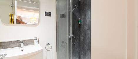 Une salle de bain moderne avec une douche à l’italienne en verre, un lavabo blanc doté d’un plan de toilette en marbre et un grand miroir au-dessus du lavabo.