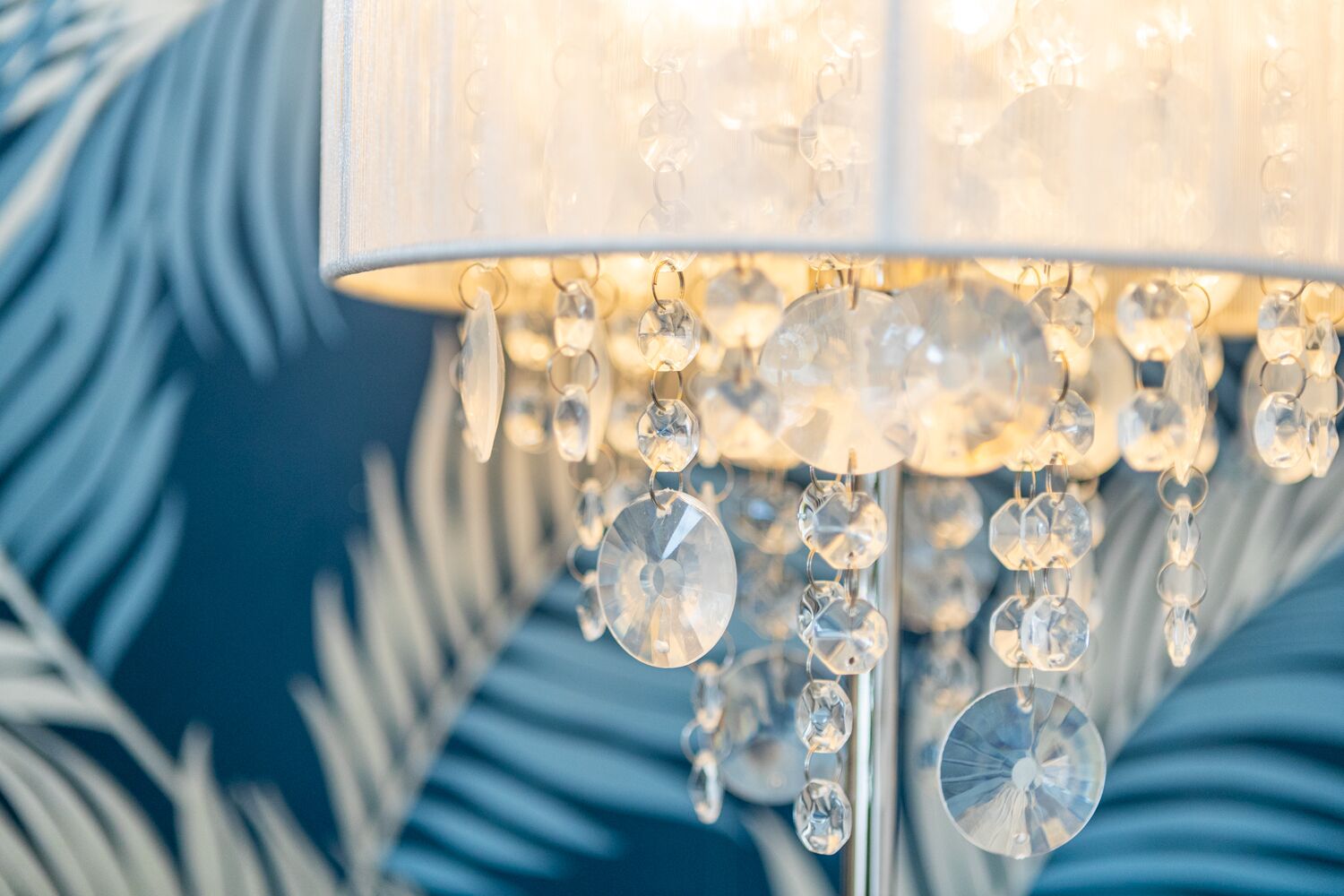 A chandelier with multiple crystal elements hanging from a white, cylindrical shade.