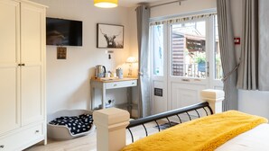 A bedroom with a bed, a desk, a chair, a bedside table, a lamp, a window with curtains, a door, and a white wardrobe. - Bowness Guest House (Windermere)