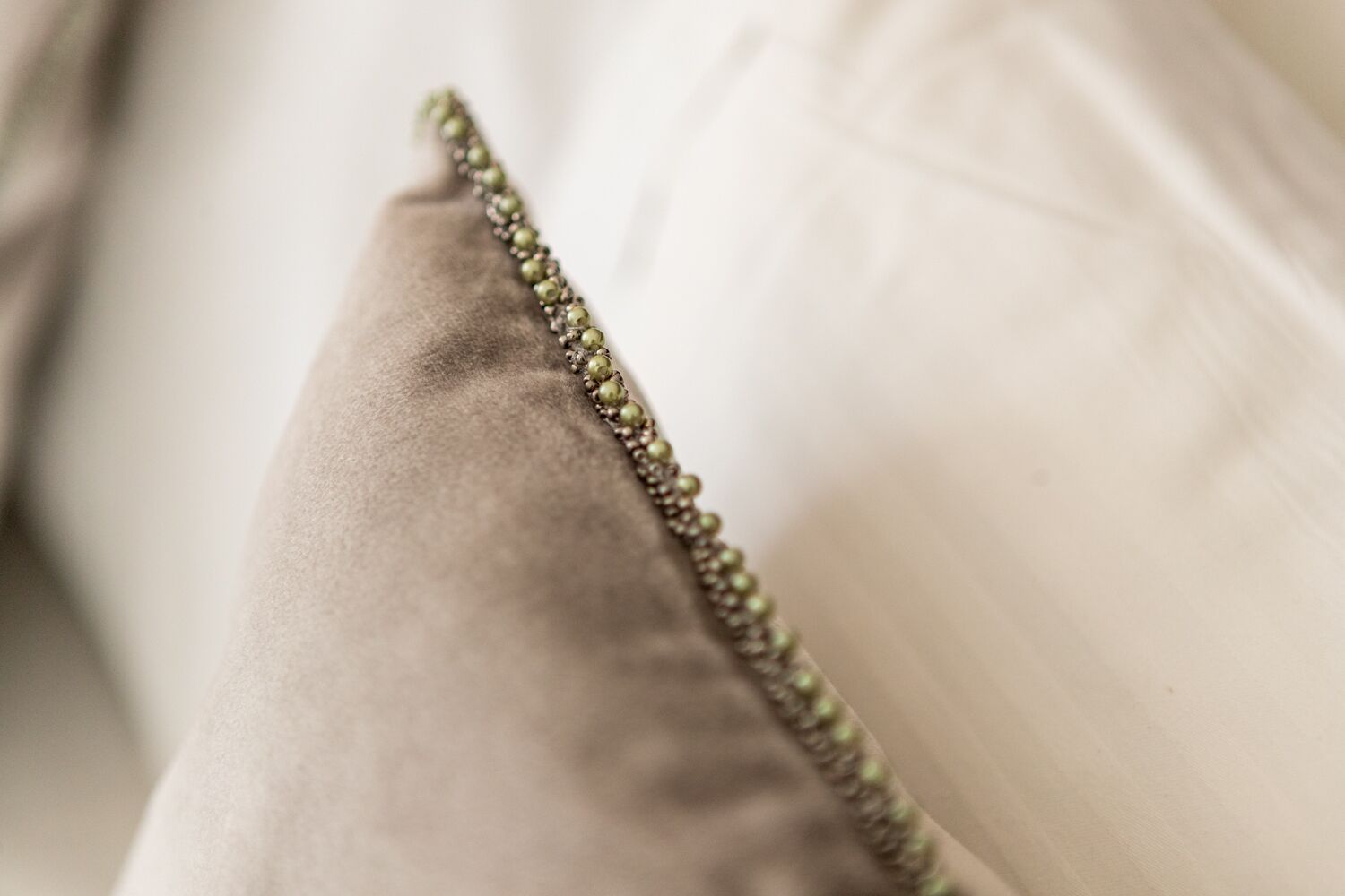 A close-up of a pillow with a textured fabric and a beaded trim.