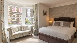 A bedroom with a large bed, a sofa, a window with a view of the city, and a small table. - Bowness Guest House (Windermere)