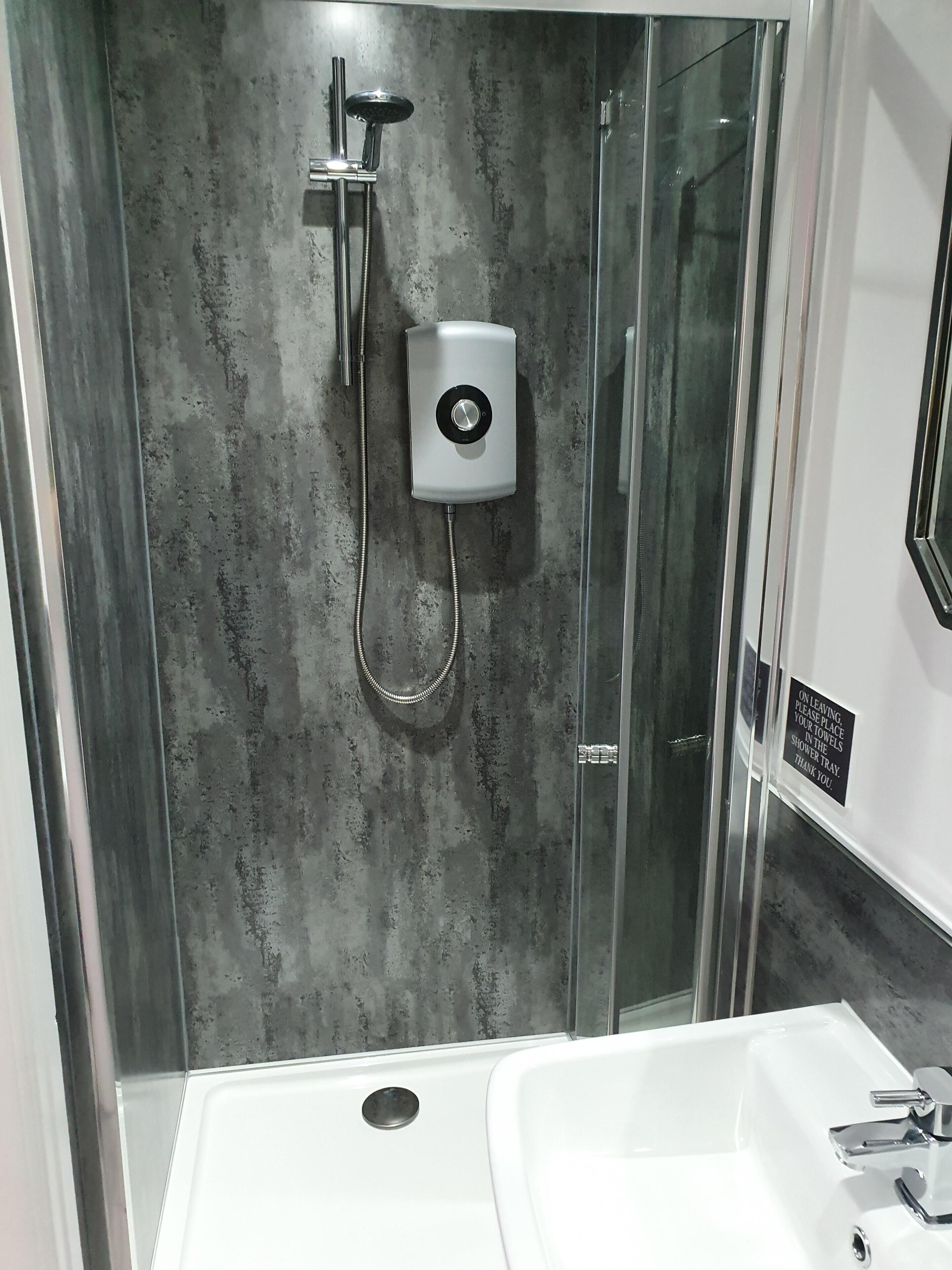 Une salle de bain moderne avec une douche à parois de verre, un lavabo blanc et un panneau de commande de douche.
