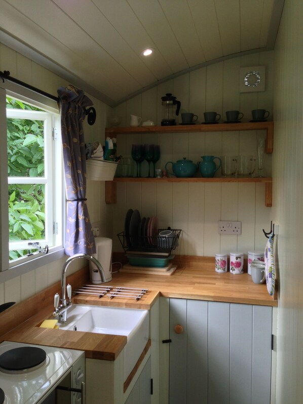 A kitchen with wooden countertops, a sink, and a stove. There are shelves above the counter holding dishes and cups. - Posh Huts (Hexham)