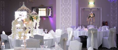 Une salle de banquet avec des tables rondes dressées pour un événement formel, des nappes blanches et des centres de table floraux.