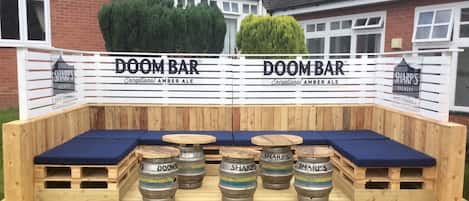 A wooden seating area with blue cushions and wooden tables, surrounded by barrels labeled 'SHARP'S DOOMBAR'.
