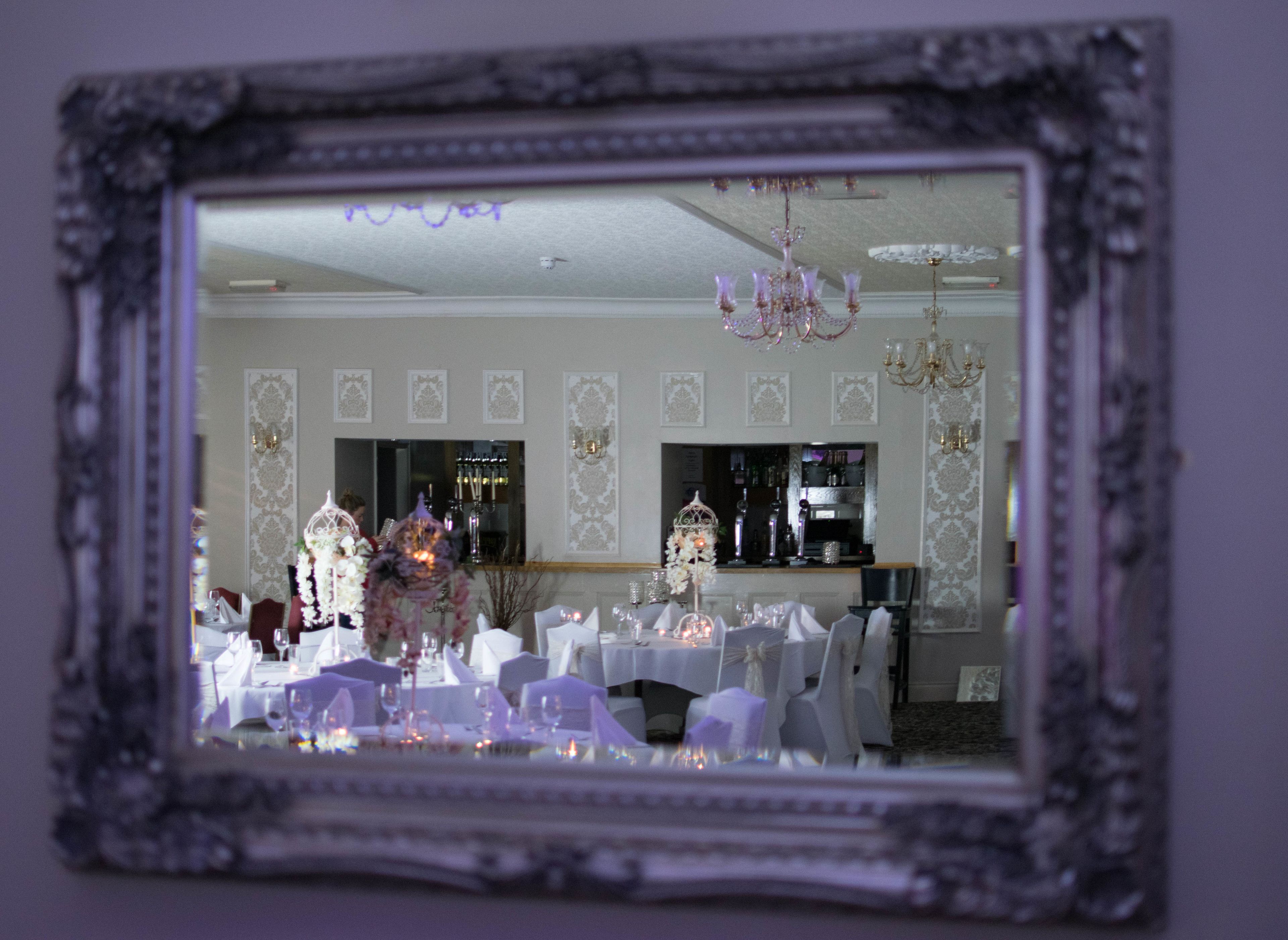A dining area with tables set for a formal event, a bar in the background, and a chandelier.