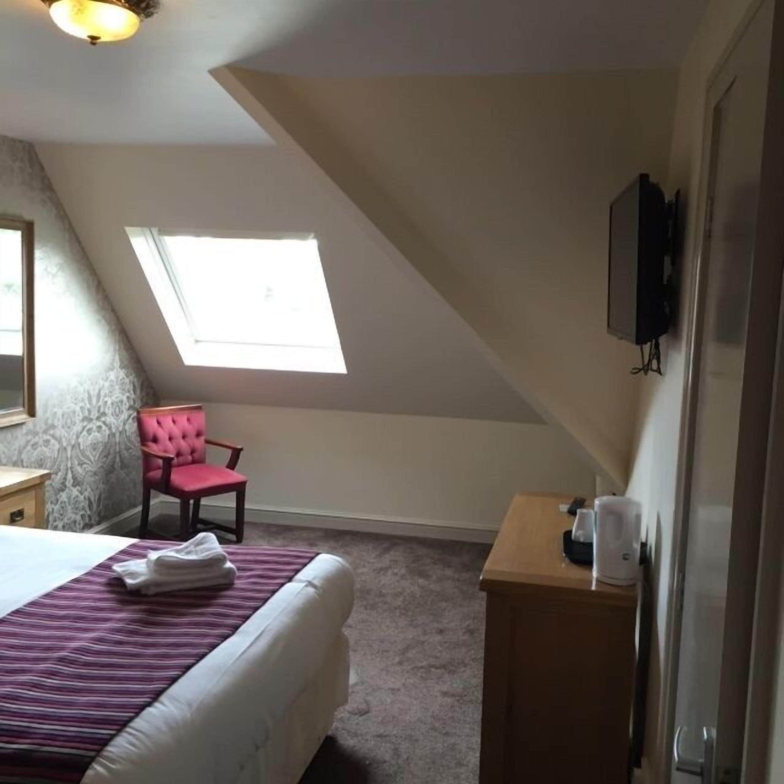 Une chambre à coucher avec un lit, une chaise, un bureau, une télévision et une fenêtre.