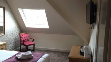 A bedroom with a bed, a chair, a desk, a television, and a window.