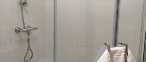 Ducha con cerramiento de vidrio, cabezal de ducha manual y toallero con dos toallas.
