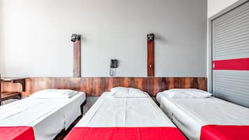 Quarto de hotel com três camas de solteiro, cabeceira de madeira, telefone e porta com listras vermelhas.