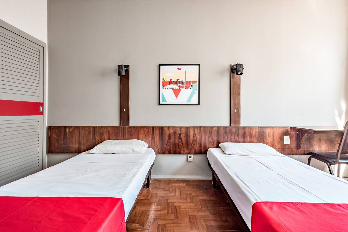 A hotel room with two single beds, a wooden headboard, a wall-mounted picture, and a wooden floor.
