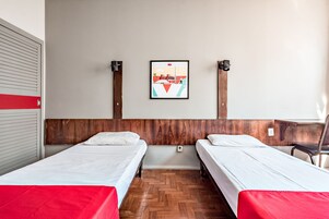 Habitación de hotel con dos camas individuales, cabecera de madera, un cuadro en la pared y suelo de madera.