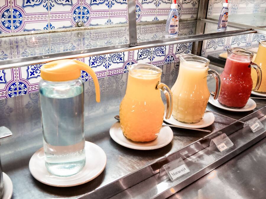 A beverage station with various drinks in pitchers and glasses, labeled with names like "Maracuja" and "Cai."