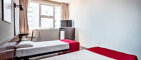 A hotel room with two beds, a TV, and a window with curtains.